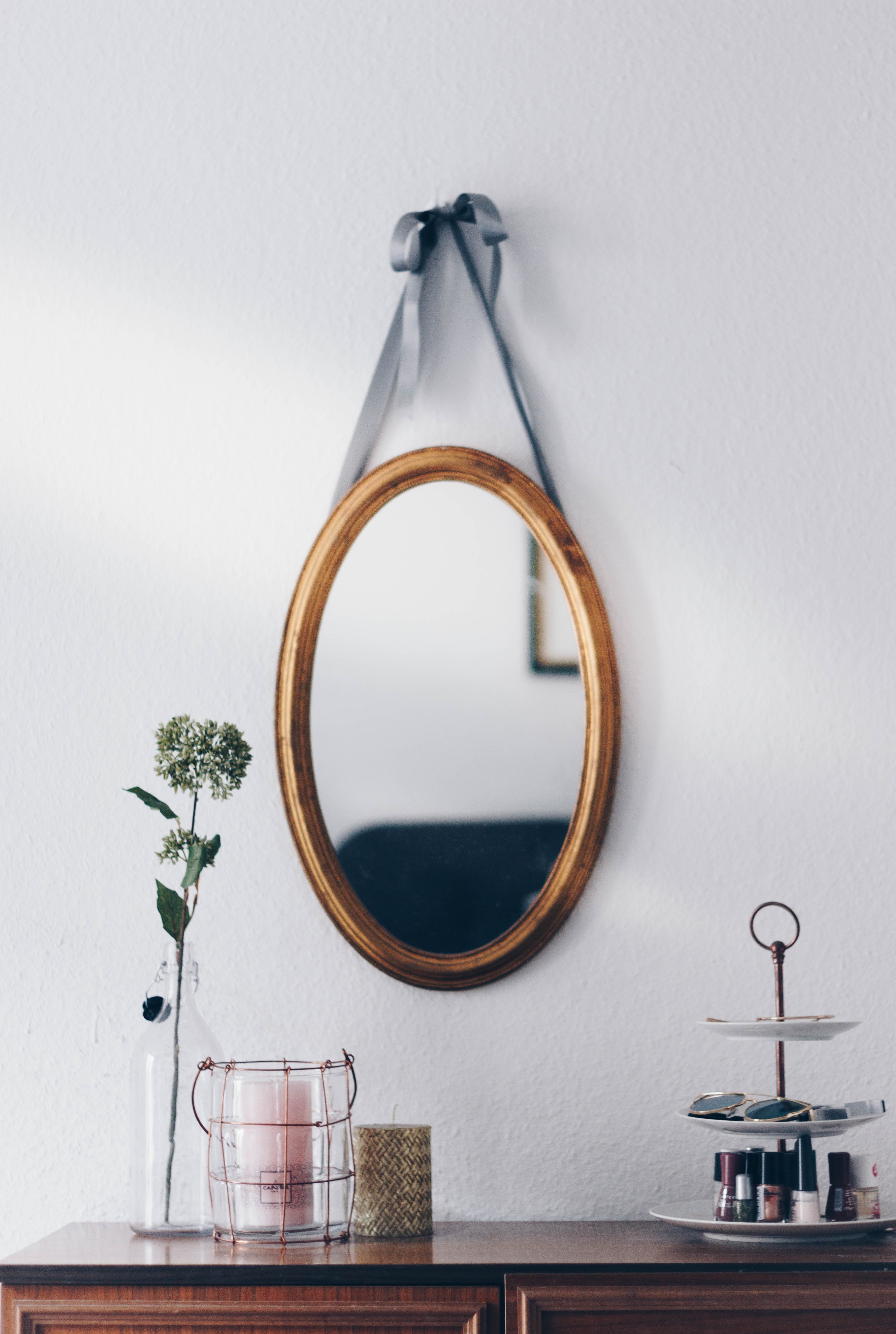an oval mirror hung from the wall and decorations sitting on a dresser