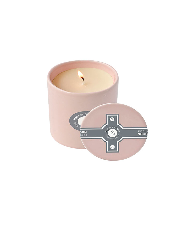A burning candle in a pink jar with a unqiue design on the lid